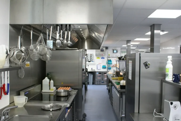 Cuisine professionnelle en inox avec plans de travail, ustensiles suspendus et allée centrale